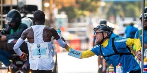 Claus-Henning Schulke hands over a bottle to double Olympic champion Eliud Kipchoge during the Berlin marathon race held in Germany